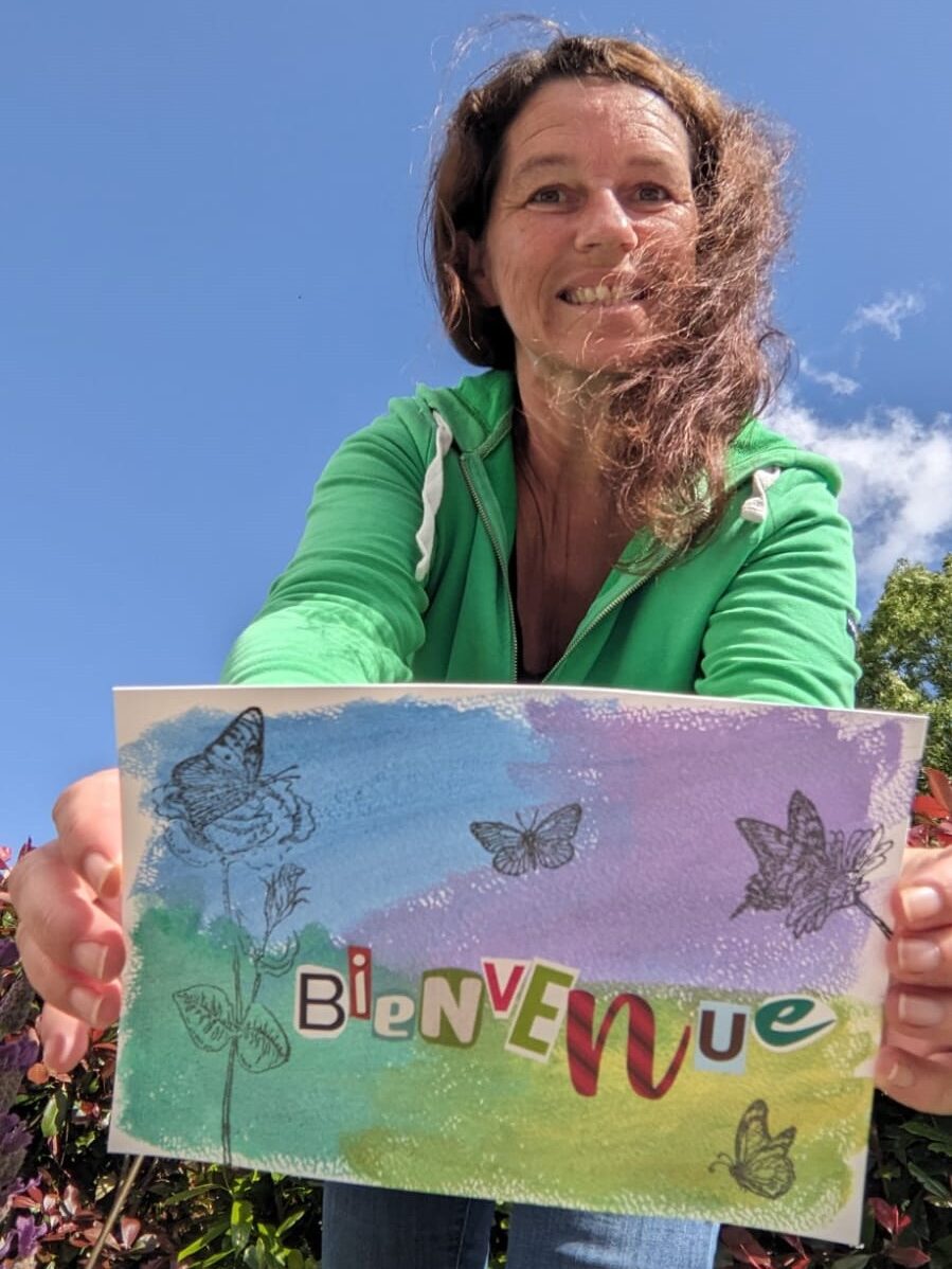 Je suis en arrière fond, et je tends les bras vers vous en vous montrant mon message de bienvenue. Les lettres bienvenues ont été découpées dans des revues, et collées sur une feuille colorée à l'aquarelle.